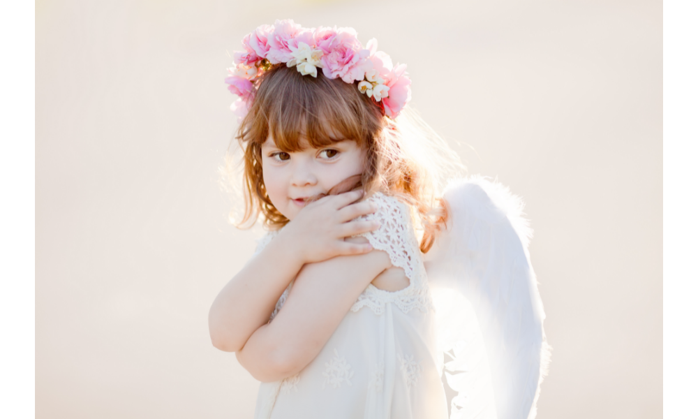 Bebê fantasiada de anjo com flores na cabeça.
