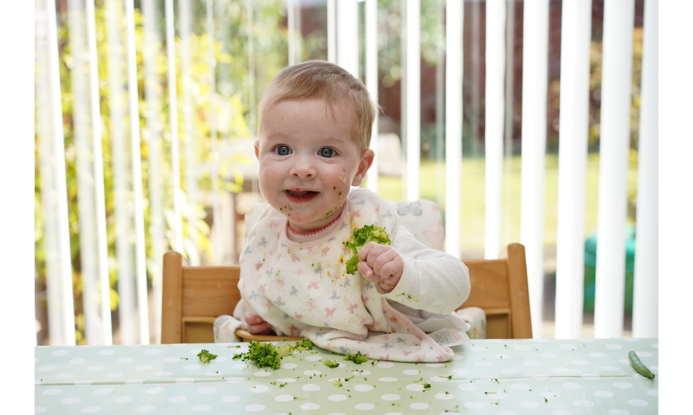 Bebê sentado em uma cadeirinha comendo brócolis.