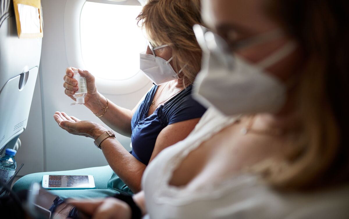 Mulheres sentadas em assento de avião com máscaras no rosto.