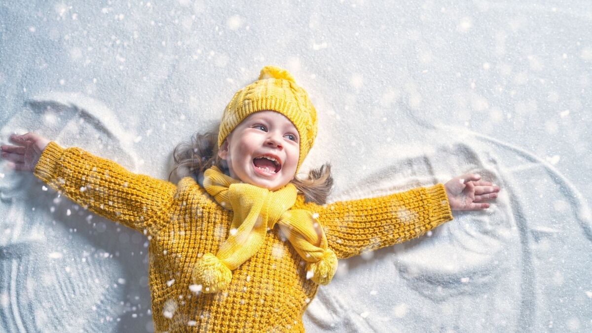 Criança fazendo asas de anjo na neve.