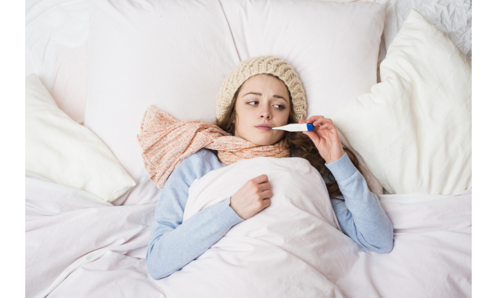 Mulher doente deitada em uma cama com um termômetro na boca.
