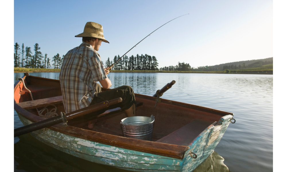 Homem sentado de costas em uma canoa com uma vara de pescar.