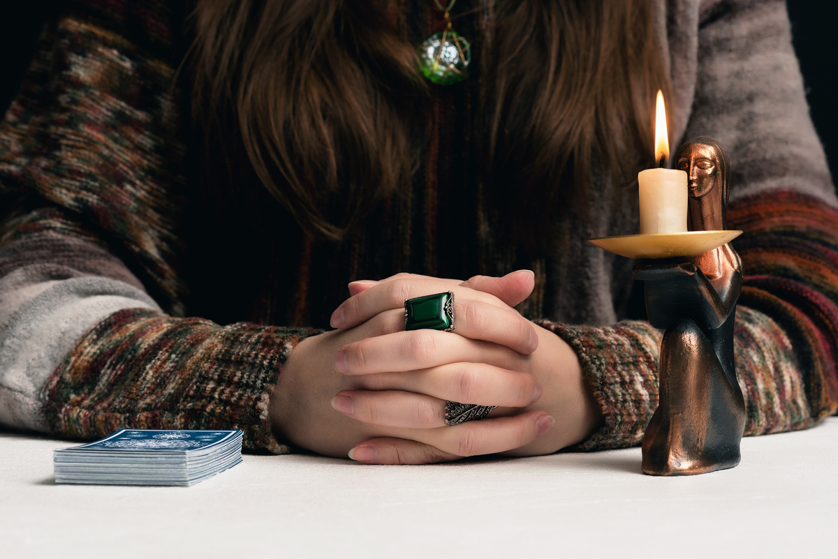 Uma mulher com as mãos entrelaçadas na mesa vela e cartas de tarot