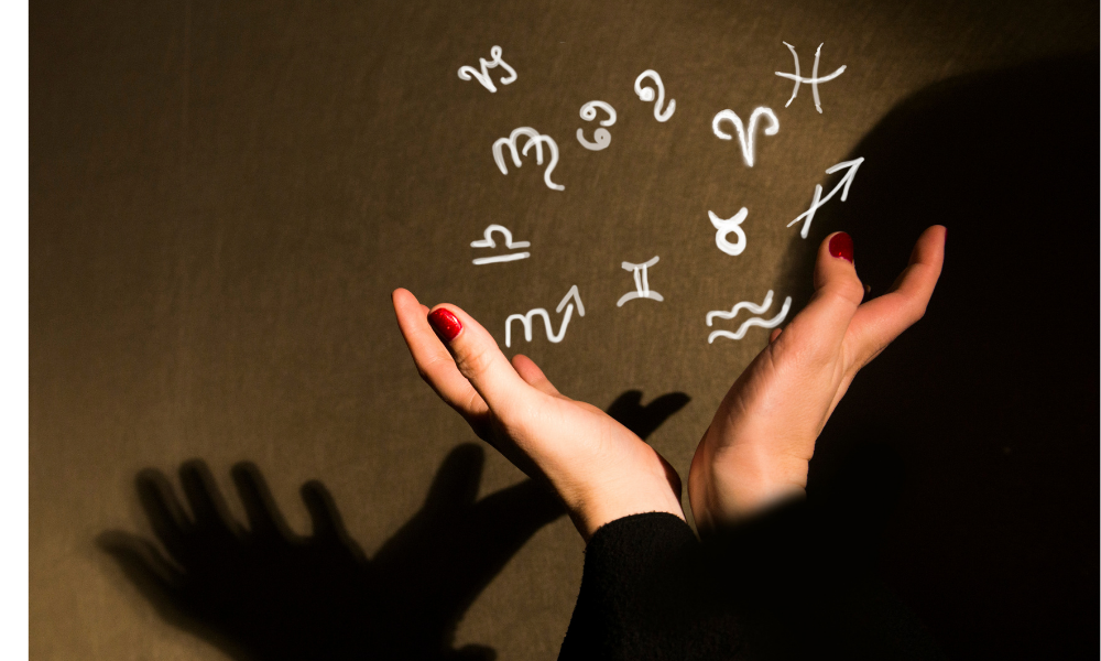 Mãos de uma pessoa com ilustrações dos símbolos do zodíaco.
