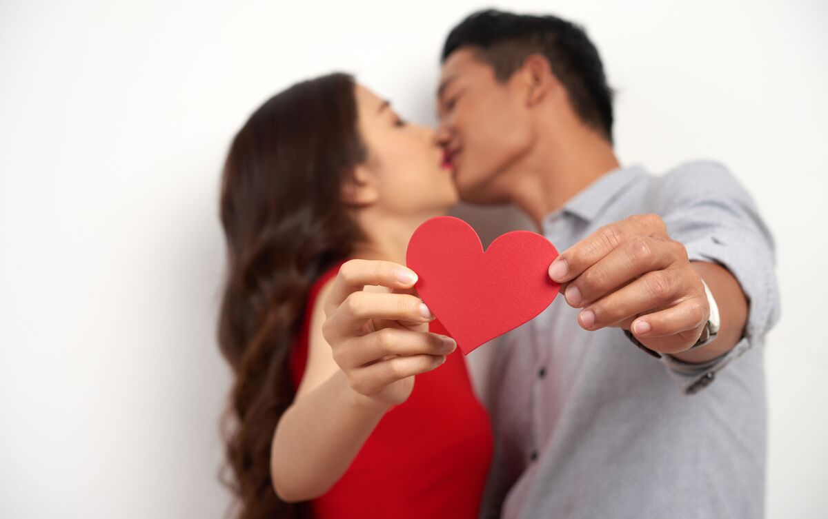 Casal de homem e mulher se beijando e segurando um coração.