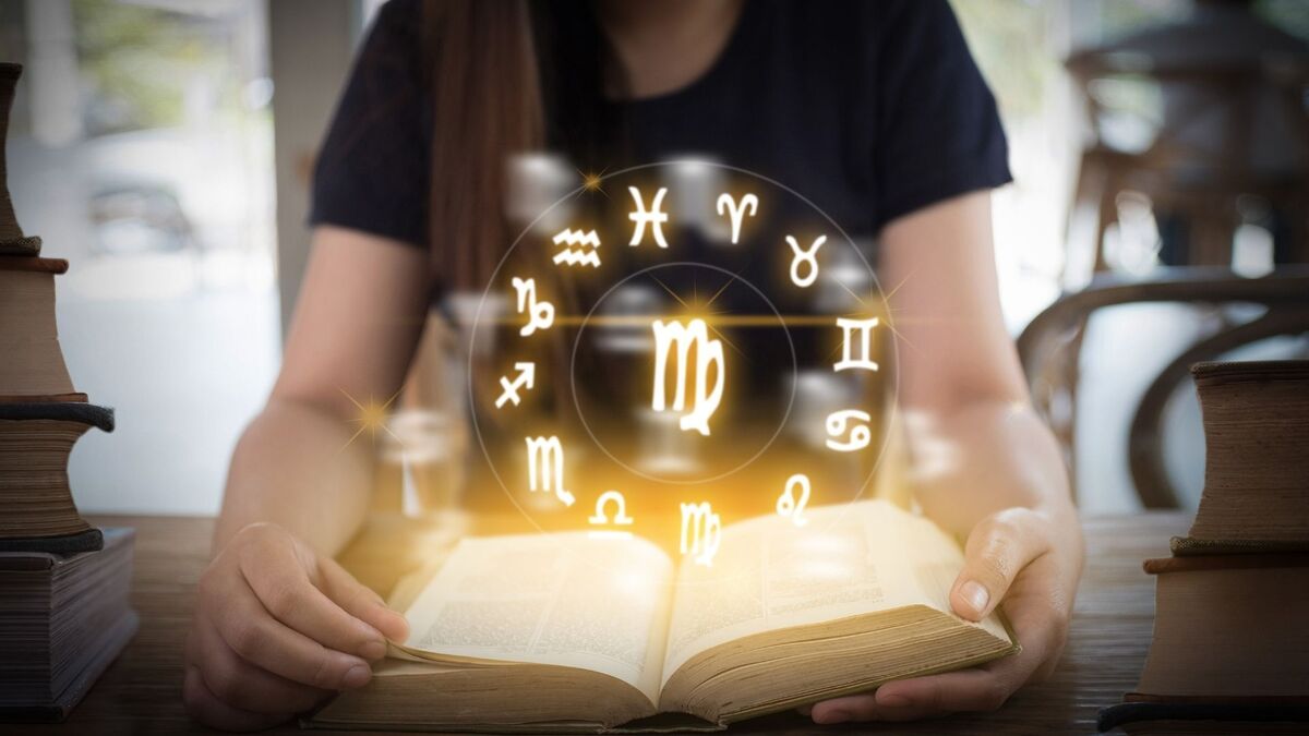 Mulher abrindo um livro com os símbolos dos signos.