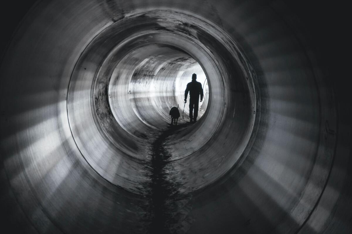 Homem andando com um cachorro em um túnel de esgoto.