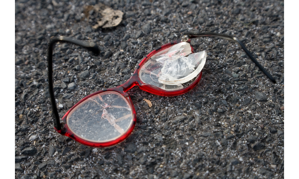 Óculos vermelho quebrado no asfalto.