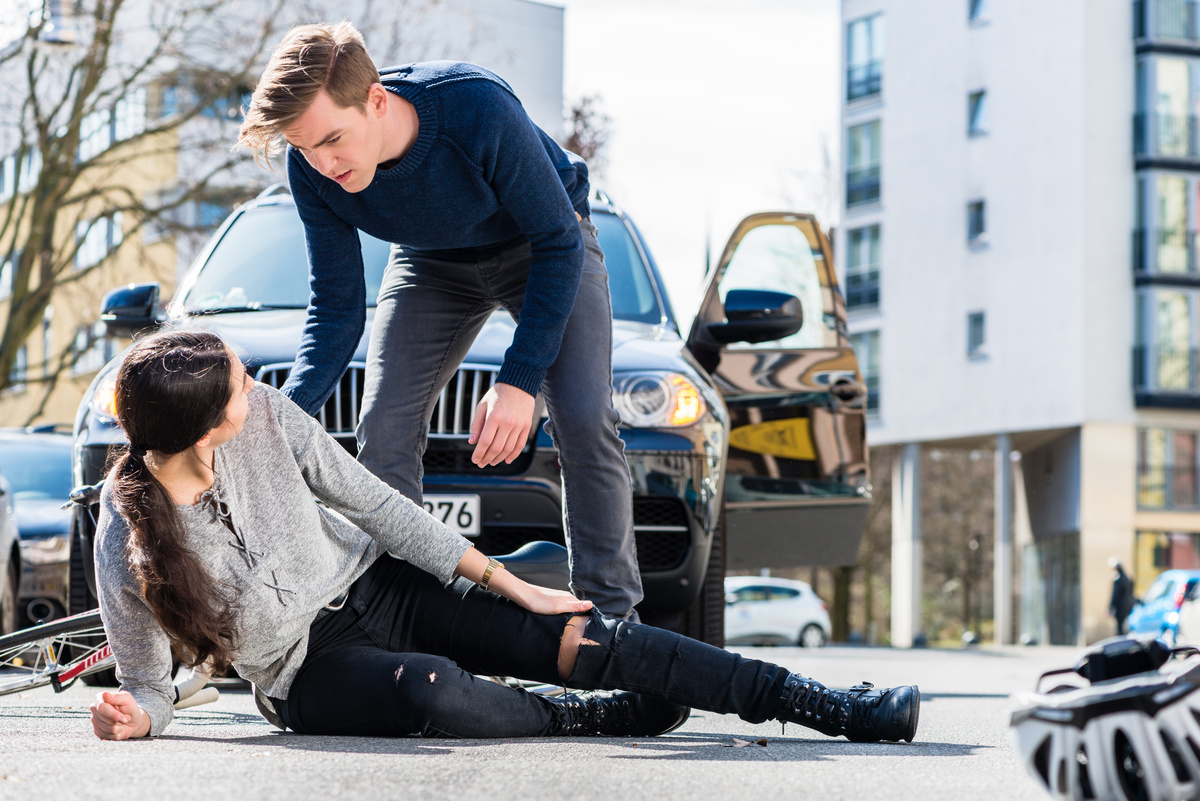 Uma moça caída no asfalto e um homem tentando ajudar