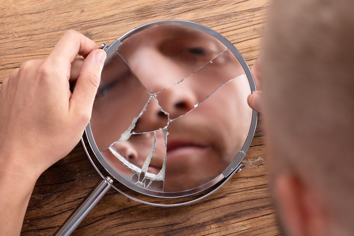 Homem vendo a sua imagem quebrada em um espelho.