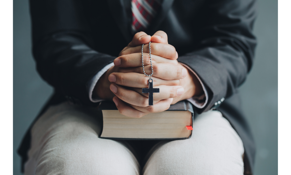 Mãos de uma pessoa em oração com um terço e bíblia.