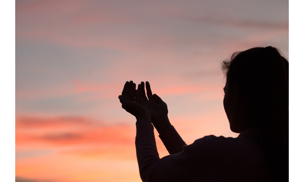 Silhueta de uma pessoa ao pôr-do-sol com as mãos estendidas ao céu.